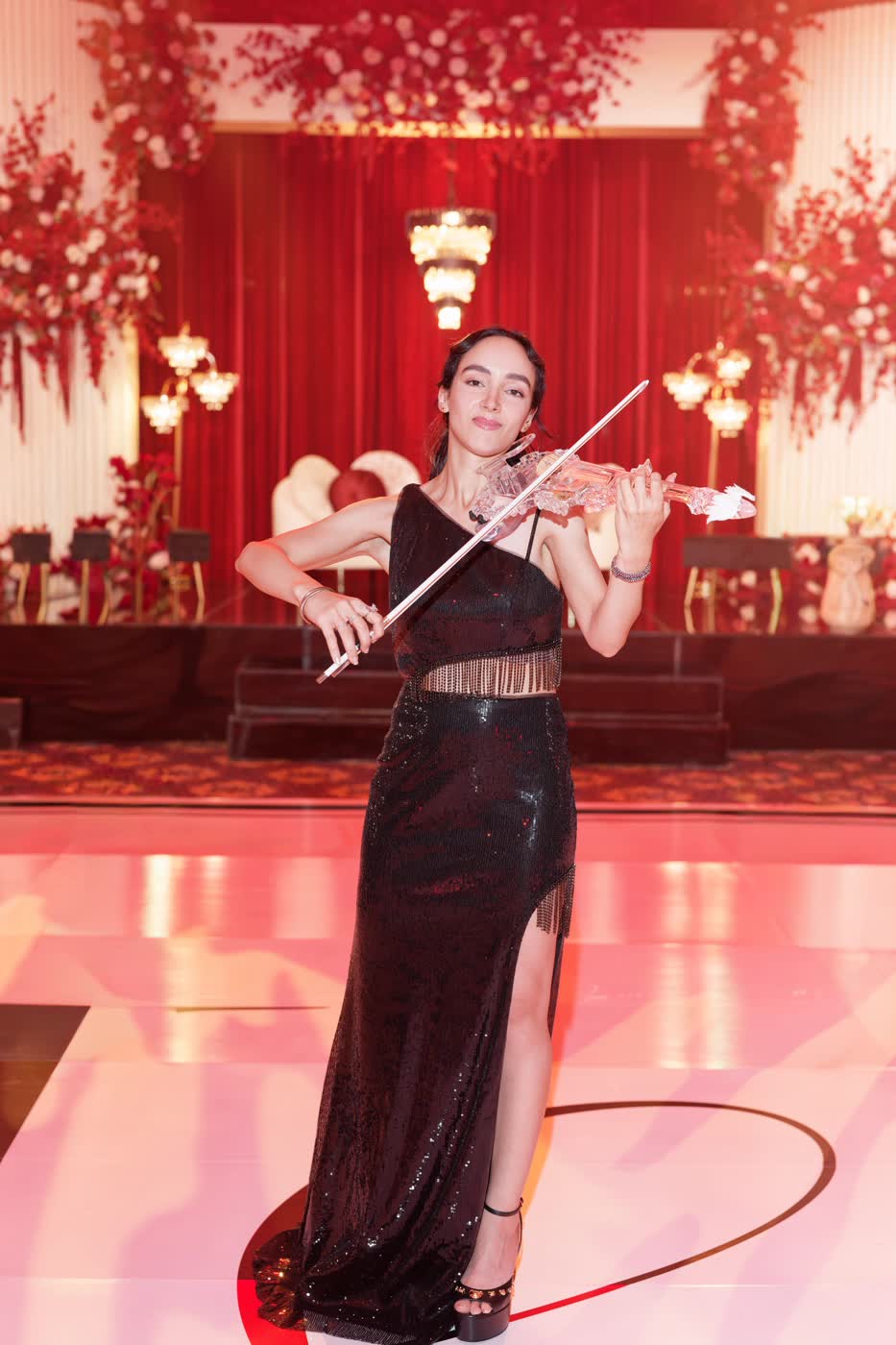 Sadie Varius playing the transparent violin on a red-lit ballroom stage at The Legacy Castle