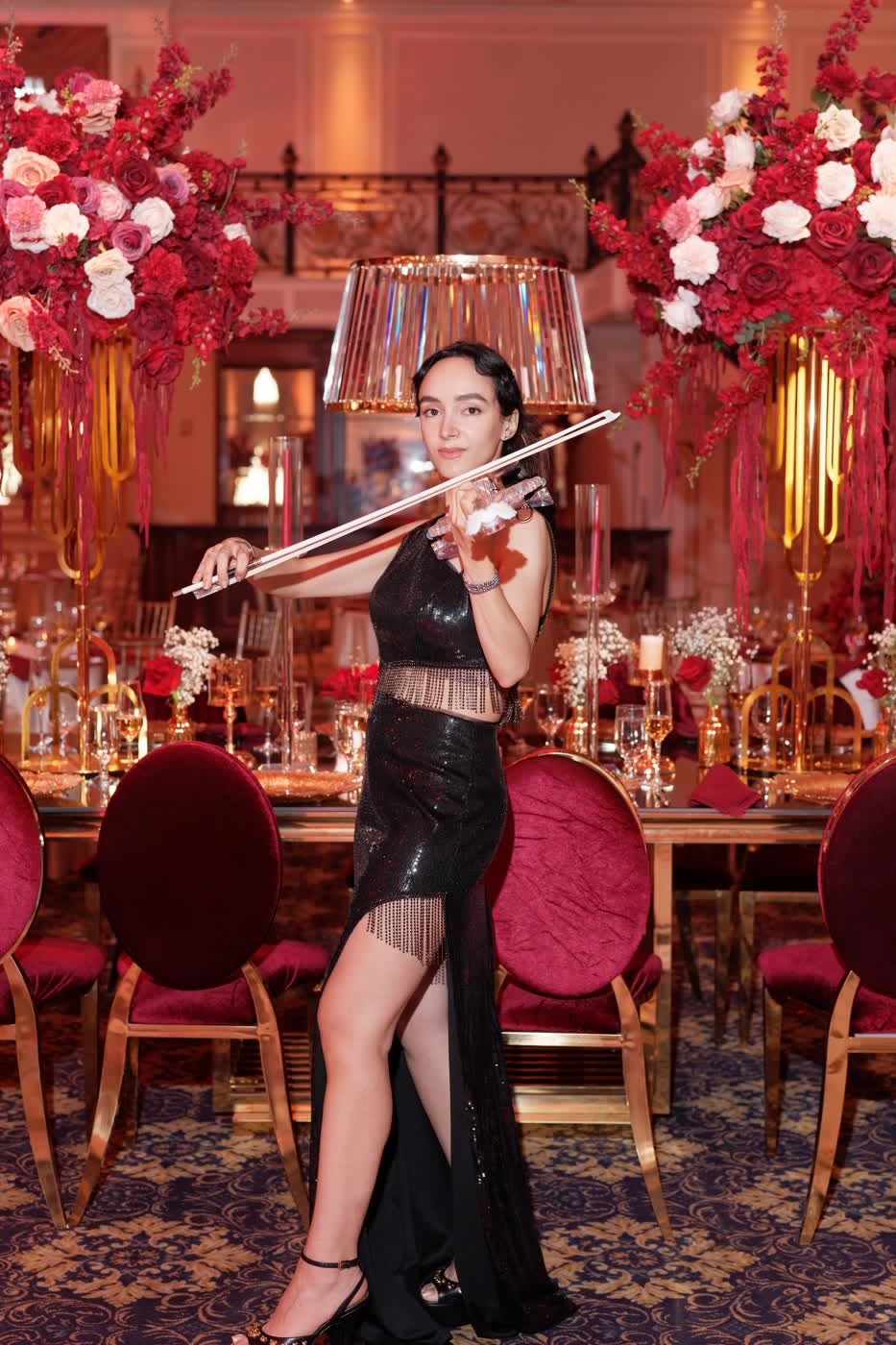 Sadie playing the transparent violin beside crimson rose arrangements at The Legacy Castle