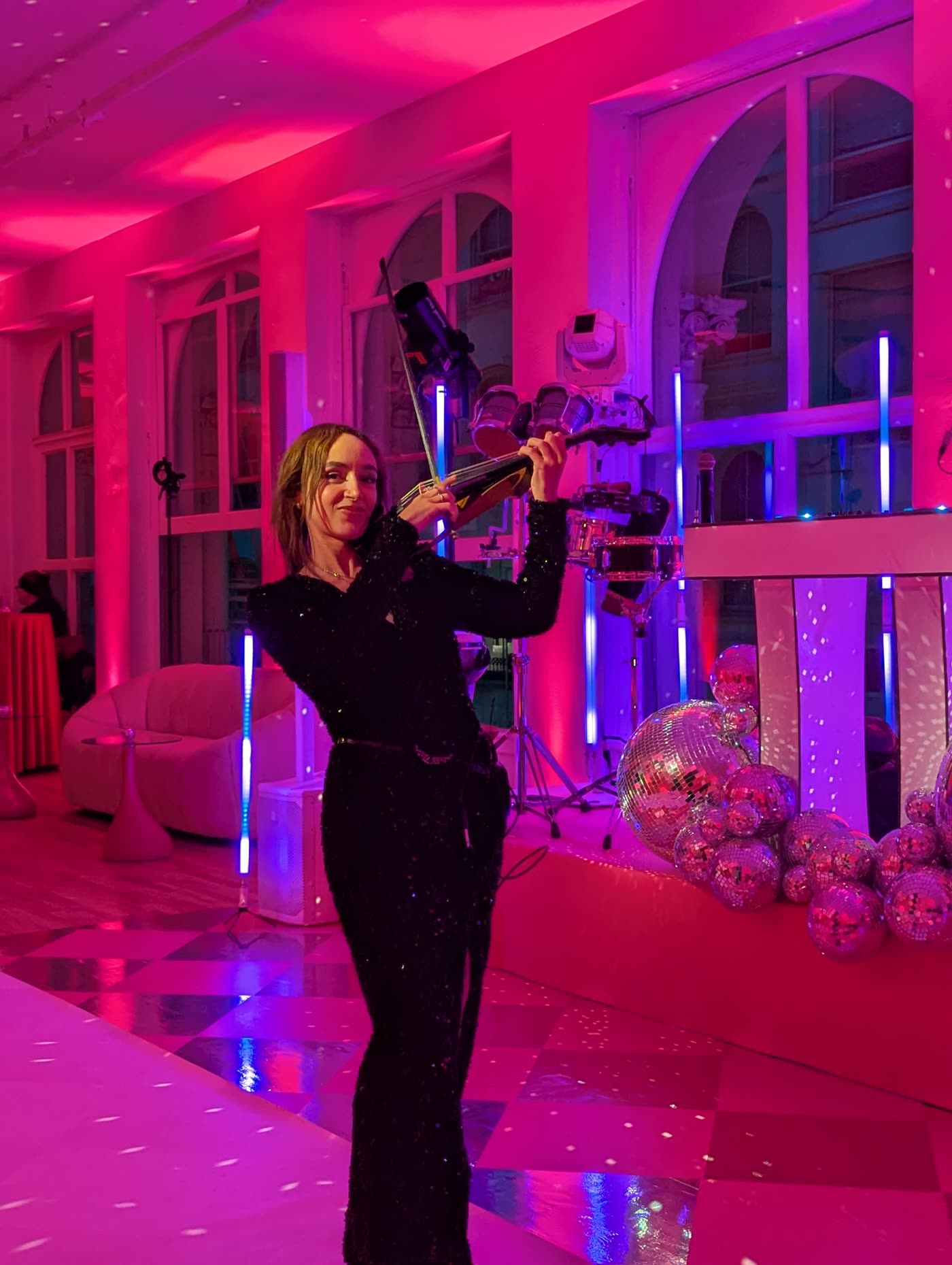 Sadie playing electric violin beside a DJ booth under disco balls